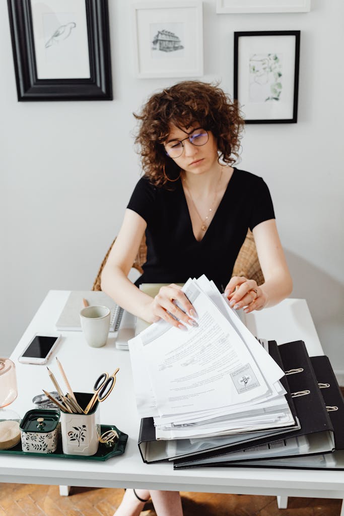 A focused woman in a black dress sorts through documents at a workspace, emphasizing productivity.